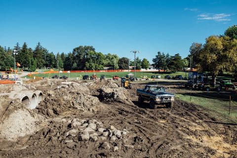 1979 Ford Bronco - A black 1970s Ford pickup truck is driving through a muddy off-road course with construction pipes and piles of dirt visible in the foregro…