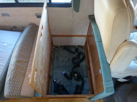 1995 Chevrolet P30 1 Ton - Step Van - Interior view of an RV showing a mattress on the left and an open storage compartment with straps on the right, next to a beige captain's c…