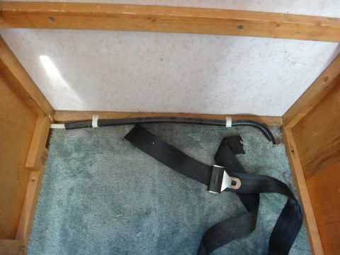 1995 Chevrolet P30 1 Ton - Step Van - A black seatbelt is laid out on a teal carpeted floor, with a black corrugated tube secured by white zip ties running along the wooden wall…