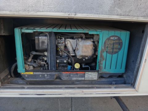 1995 Chevrolet P30 1 Ton - Step Van - A close-up view of a generator unit installed in an RV compartment. The generator has a teal-colored housing with a "NEW!" sticker and visi…