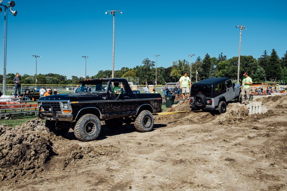 Black Ford Bronco pulling a silver Jeep Wrangler through a dirt obstacle course.