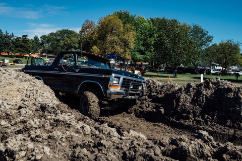 1979 Ford Bronco - A black 1970s Ford Bronco is navigating a challenging mud pit, with large tires digging into the thick, brown mud. The vehicle is angled up…