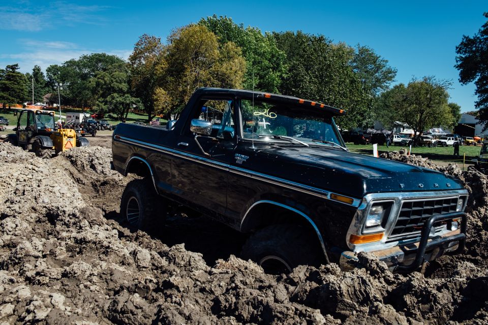 Black 1979 Ford Bronco stuck in mud pit with yellow tractor in background.