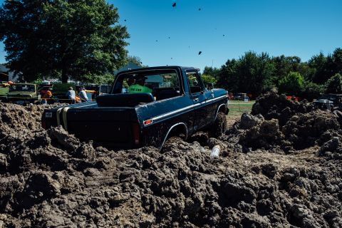 1979 Ford Bronco - A dark blue Ford Bronco is stuck in a large pile of mud, with two people visible in the cab. The vehicle appears to be participating in a m…