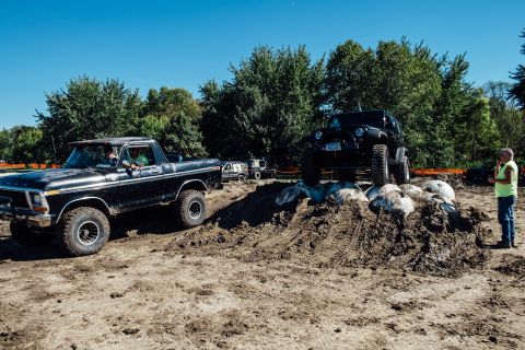 1979 Ford Bronco - A black 1979 Ford Bronco is shown driving on a dirt track with a black Jeep Wrangler on a mound of dirt and rocks in the background. A man…