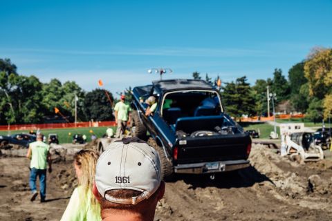 1979 Ford Bronco - A black Ford pickup truck is positioned on a dirt mound with its rear facing the camera. People are gathered around watching the truck, wit…