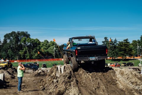 1979 Ford Bronco - A black Ford pickup truck with large tires navigates an off-road obstacle course, climbing a steep dirt ramp under a clear blue sky. The tr…