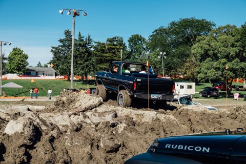 1979 Ford Bronco - A black 1970s Ford Bronco is driving through a muddy obstacle course on a sunny day. The vehicle is lifted and has large tires, indicating…