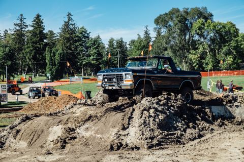 1979 Ford Bronco - A black Ford pickup truck with a lifted suspension navigates an off-road obstacle course made of dirt and mud. The truck is angled upwards…