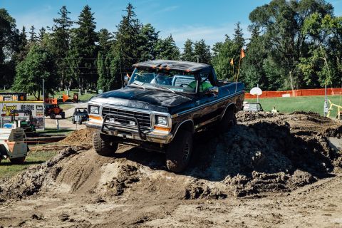 1979 Ford Bronco - A black 1979 Ford Bronco is driving up a dirt mound in an outdoor event. The vehicle has a lifted suspension and off-road tires.