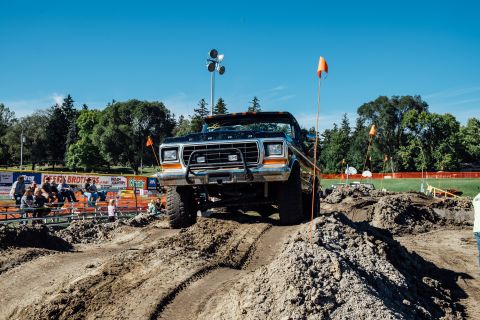 1979 Ford Bronco - A lifted, black and orange Ford Bronco is shown navigating a dirt obstacle course with spectators in the background.