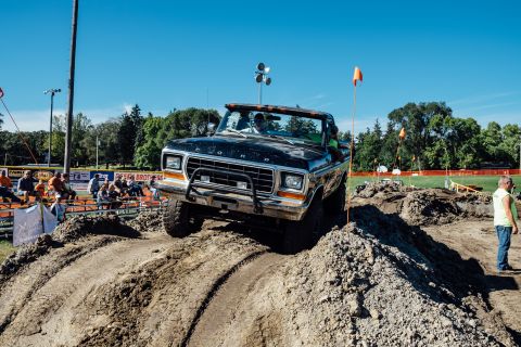 1979 Ford Bronco - A black 1970s Ford truck with a lifted suspension navigates a dirt obstacle course with spectators in the background.