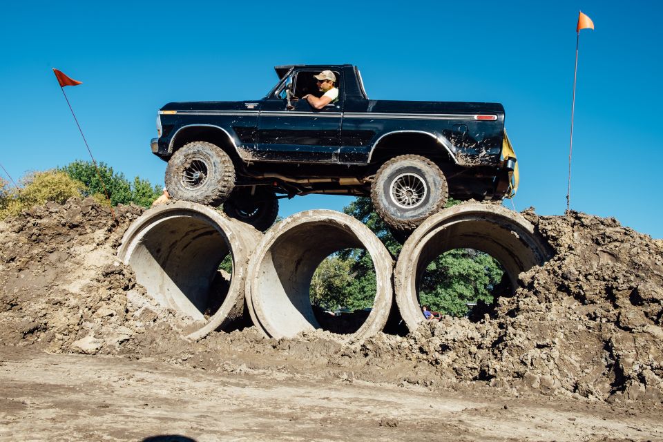 Black 1979 Ford Bronco driving over concrete pipes on a dirt mound.