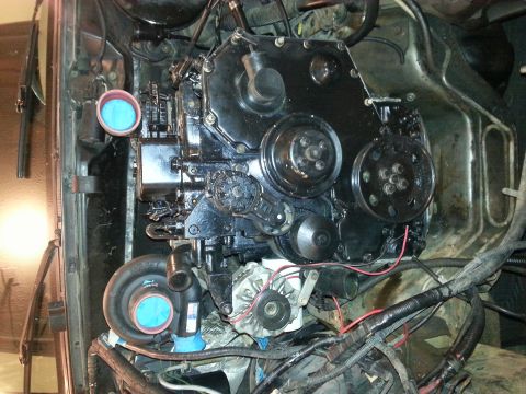 1994 Ford Bronco - A close-up view of a black engine, likely a diesel, with a turbocharger visible on the left side. Blue filters are covering the intake port…