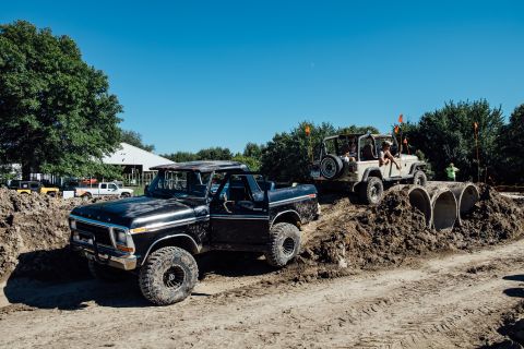 1979 Ford Bronco - A black 1979 Ford Bronco is parked in a dirt track obstacle course, with a tan Jeep Wrangler navigating a mound of dirt and concrete pipes…