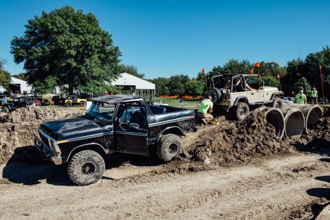 1979 Ford Bronco - A black Ford Bronco navigates an off-road obstacle course, with a tan Jeep Wrangler following behind. The course features dirt mounds and l…