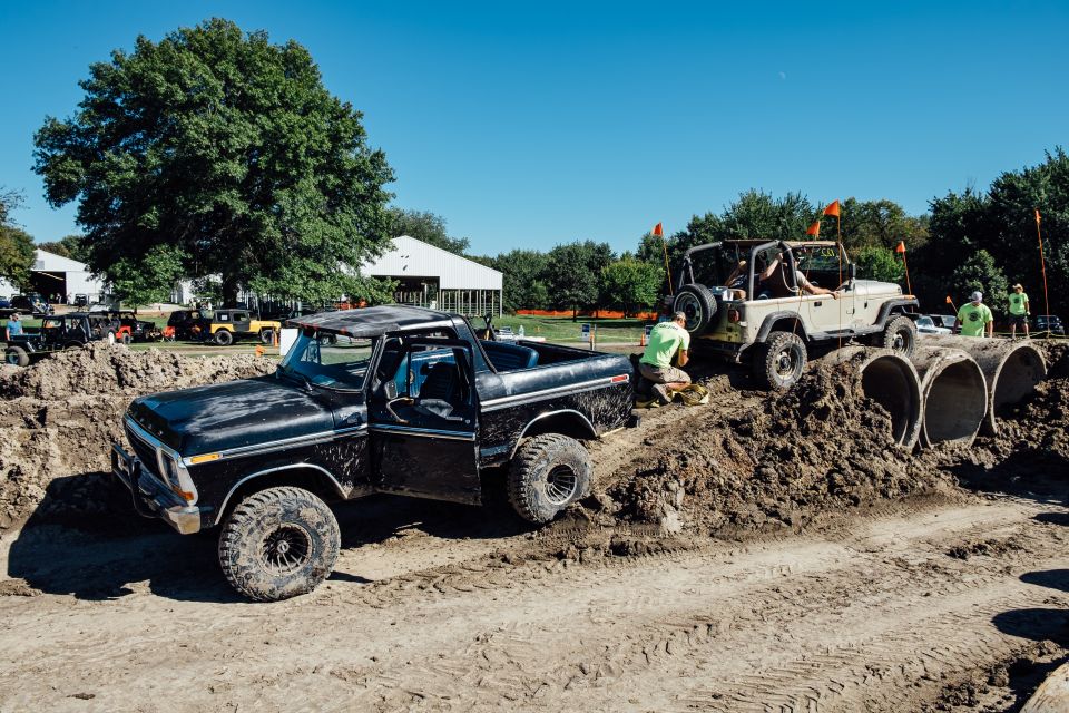 Black 1970s Ford Bronco driving through a dirt obstacle course with a tan Jeep Wrangler.