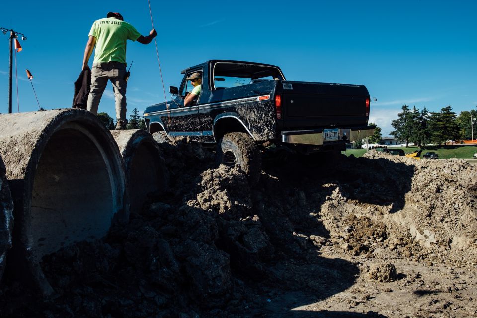 Black 1970s Ford pickup truck driving over a dirt obstacle course with concrete pipes.