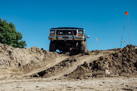 1979 Ford Bronco - A lifted, dark-colored Ford Bronco is positioned on a dirt mound, facing the camera. The vehicle is surrounded by a muddy, off-road terrain…