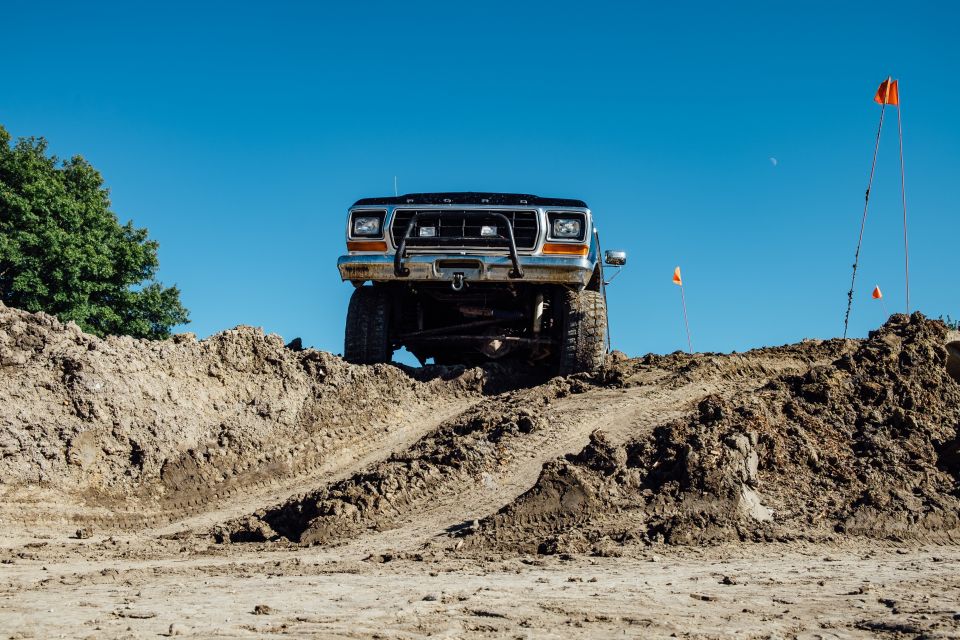 Lifted Ford Bronco on a dirt mound with orange flags in the background.