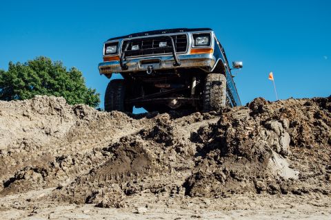 1979 Ford Bronco - A dark-colored Ford Bronco is angled up a steep dirt embankment under a clear blue sky. The front of the vehicle is visible, showing its gr…