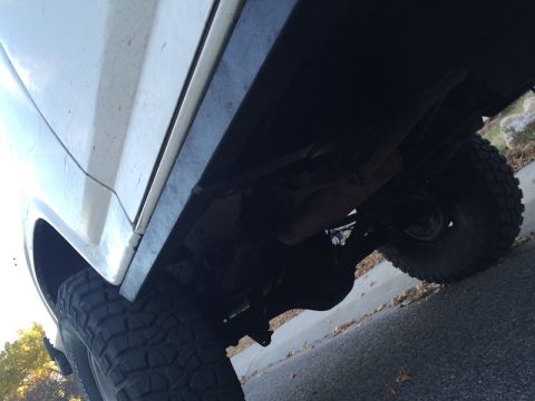 1981 Ford Bronco - Low angle shot of the underside of a white vehicle, focusing on the wheel well and suspension components. The vehicle appears to be an olde…