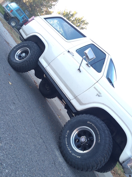 1981 Ford Bronco - A white 1980s Ford Bronco is parked on a street, angled towards the viewer's right. The vehicle features large BFGoodrich Mud-Terrain T/A t…