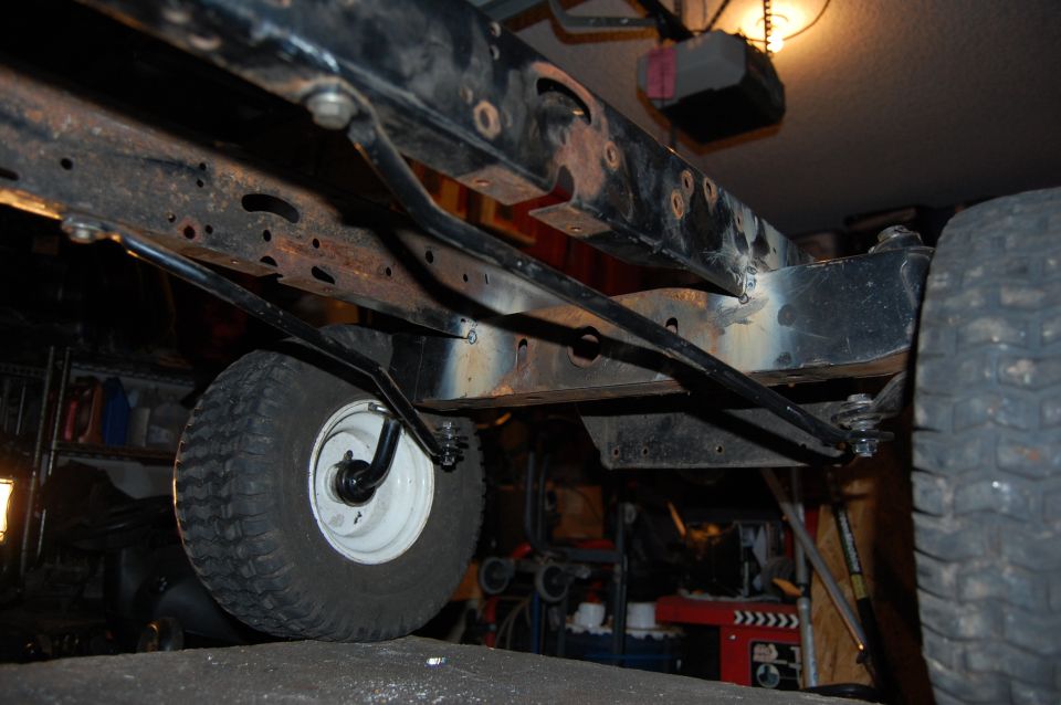 Underside of a rusty black vehicle frame with tire and suspension