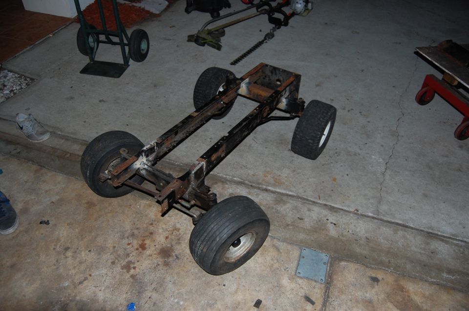Rusty metal go-kart frame with four wheels on concrete.