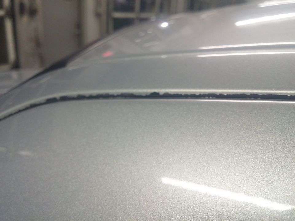 Close-up of a silver hood and fender body seam