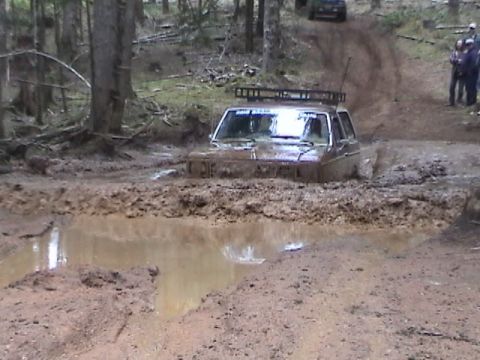 1994 Ford Explorer - A brown SUV navigates a muddy trail, getting stuck in a deep puddle with a second vehicle visible further up the path.