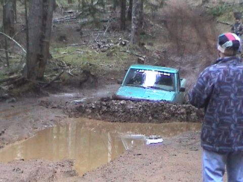 1994 Ford Explorer - A turquoise pickup truck is stuck in a muddy puddle in a wooded area.