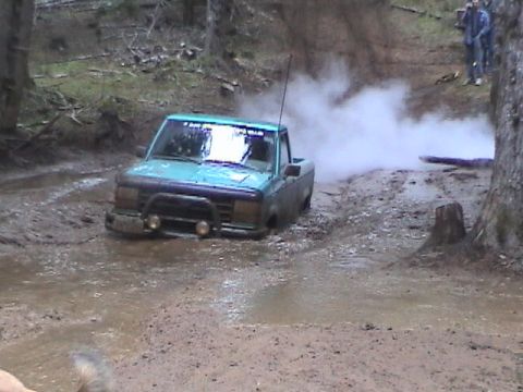 1994 Ford Explorer - A teal pickup truck is stuck in a muddy trail, with smoke billowing from its rear.