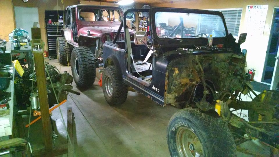 Two Jeep CJ-style vehicles in a garage, one red and one black, undergoing modification.
