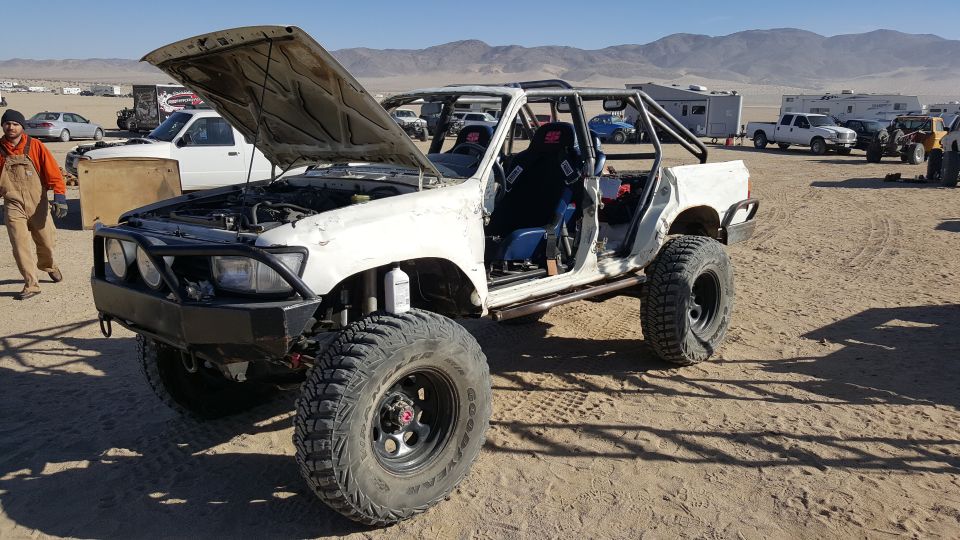 Modified white Toyota 4Runner with roll cage and large tires in a desert setting.
