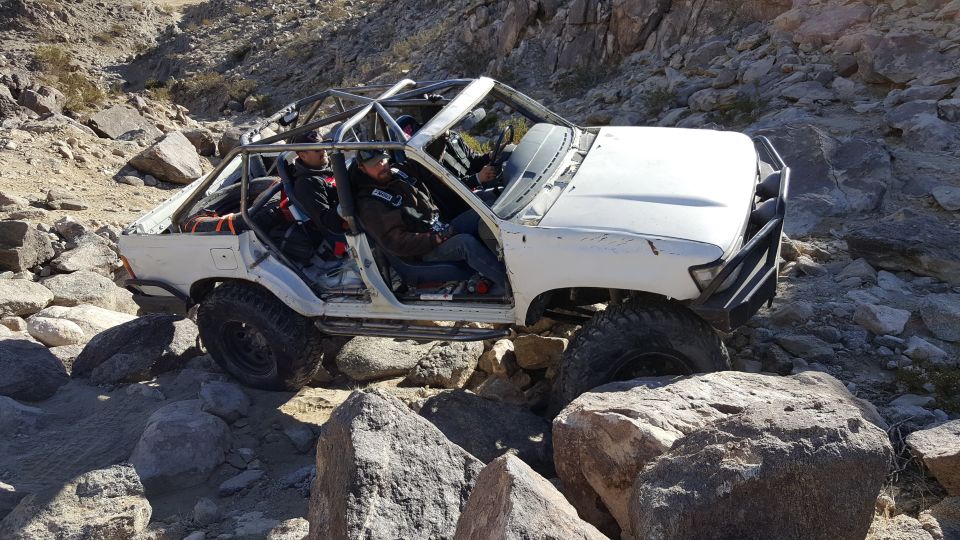 Modified white Toyota 4Runner with roll cage on a rocky off-road trail.