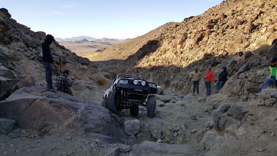 White Toyota 4Runner off-roading on a rocky desert trail with people watching.