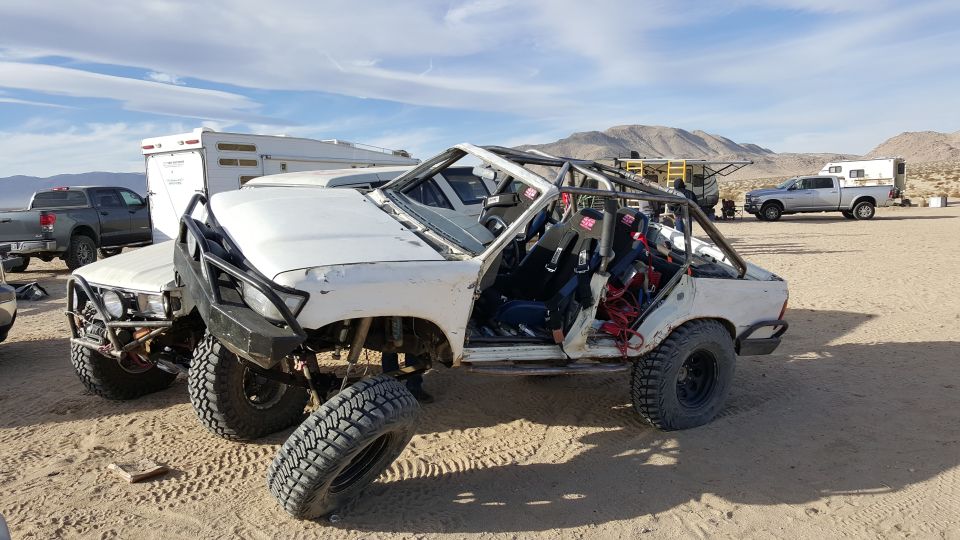 Modified white Toyota 4Runner with roll cage and off-road tires in a desert setting.