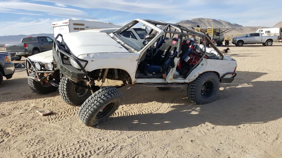 Modified white Toyota 4Runner with roll cage and racing seats in a desert setting.