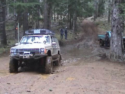 1994 Ford Explorer - A lifted Jeep Cherokee XJ navigates a muddy trail with another truck in the background.