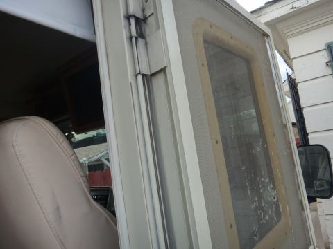 1995 Chevrolet P30 1 Ton - Step Van - Close-up view of the exterior screen door of a step van, showing the mesh screen and frame. The interior of the vehicle with a beige seat i…