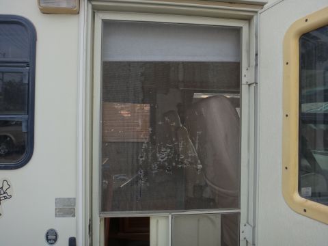 1995 Chevrolet P30 1 Ton - Step Van - A close-up view of a damaged screen door on a recreational vehicle. The screen has several tears and holes, revealing the interior of the v…