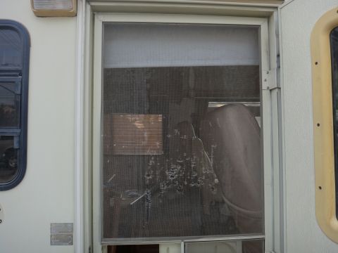 1995 Chevrolet P30 1 Ton - Step Van - A close-up view of a damaged screen door on a step van. The screen has multiple tears and holes, revealing the interior of the vehicle incl…