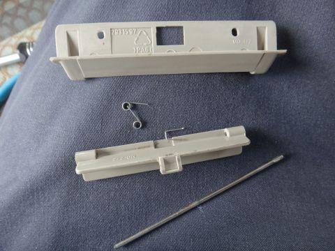 1995 Chevrolet P30 1 Ton - Step Van - A disassembled plastic component with a metal spring and rod, likely from a vehicle interior part, is laid out on a dark blue fabric surfac…