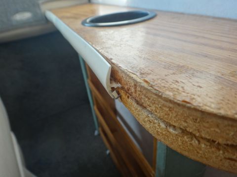 1995 Chevrolet P30 1 Ton - Step Van - A close-up view of the edge of a wooden countertop with a white plastic trim strip attached. The countertop has a circular cutout for a cup…