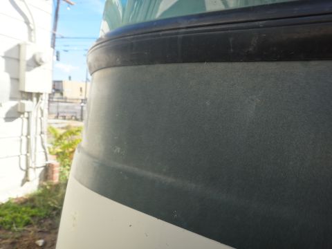 1995 Chevrolet P30 1 Ton - Step Van - Close-up view of the upper body of a step van, showing a dark gray textured panel with a black trim piece above it. A white stripe is visib…