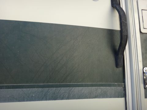 1995 Chevrolet P30 1 Ton - Step Van - A close-up view of a dark green panel on a vehicle's exterior, showing numerous scratches. A black rubber handle is visible on the right si…