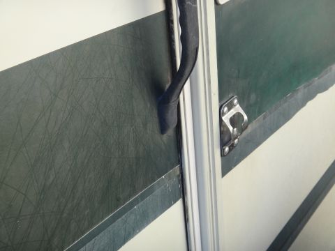 1995 Chevrolet P30 1 Ton - Step Van - A close-up view of a dark green and white striped surface on a vehicle, featuring a black handle and a metal latch. The green surface shows…