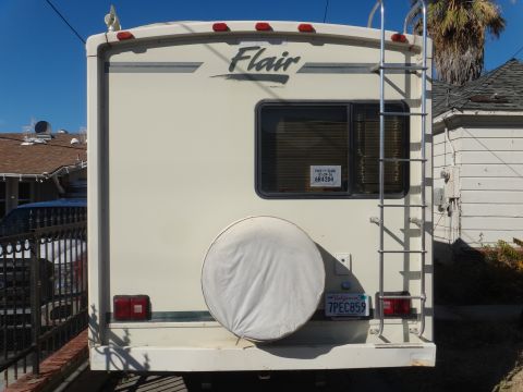 1995 Chevrolet P30 1 Ton - Step Van - The rear of a cream-colored RV is shown, featuring a spare tire cover, a ladder, and a California license plate reading "7PEC859". A small…