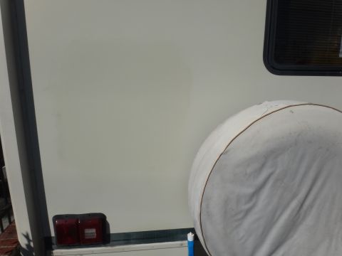 1995 Chevrolet P30 1 Ton - Step Van - White camper or trailer body panel with a covered spare tire and red marker lights at lower edge.